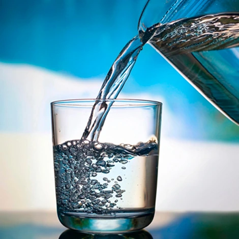 De l'eau est versée dans un verre d'eau, à l'aide d'un pichet, ce qui produit des bulles.